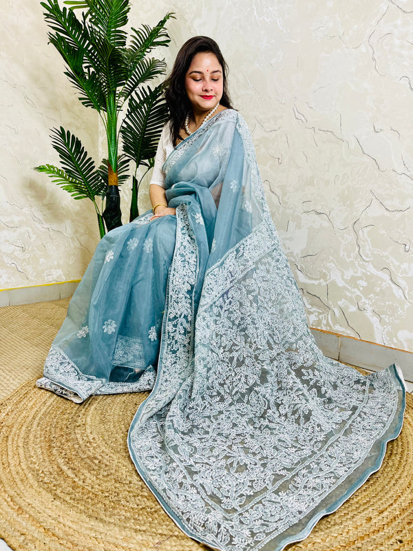 Handmade Lucknowi Chikankari pastel dusty blue pure organza silk saree with dense white jaal and floral embroidery — sitting drape view, Desi Aadat