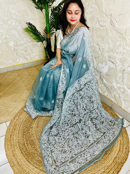 Handmade Lucknowi Chikankari pastel dusty blue pure organza silk saree with dense white jaal and floral embroidery — sitting drape view, Desi Aadat