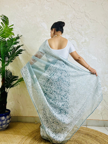 Pastel powder blue Chikankari handstitched organza silk saree with full white jaal embroidery displayed on standing model — pallu view, Desi Aadat