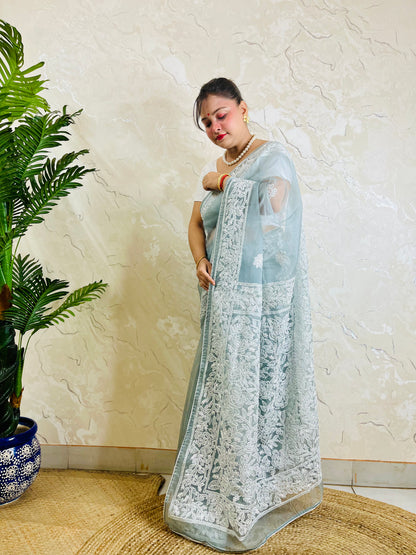 Pastel powder blue Chikankari handstitched organza silk saree with full white jaal embroidery displayed on standing model — pallu view, Desi Aadat