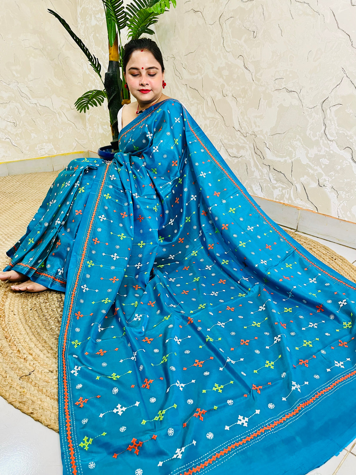 Seated pose in peacock blue saree showing Kutch embroidery pallu spread on silk