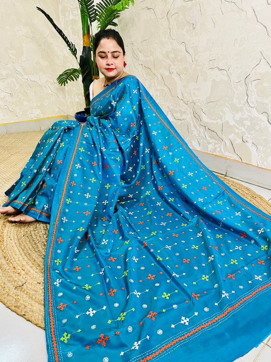 Seated pose in peacock blue saree showing Kutch embroidery pallu spread on silk