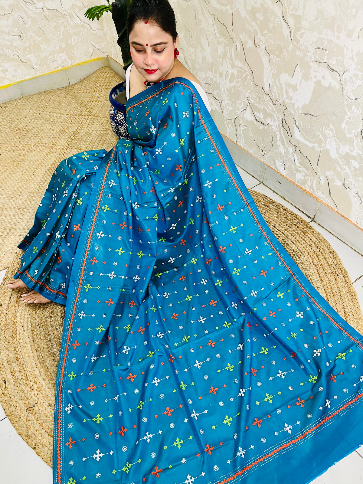Seated pose in peacock blue saree showing Kutch embroidery pallu spread on silk