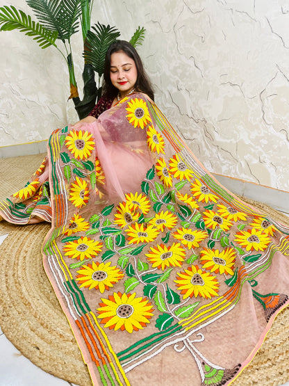 Handmade sunflower Kantha stitch blush pink organza saree with large golden yellow sunflower blooms and multicolour stripe border — angled sitting drape view, Desi Aadat