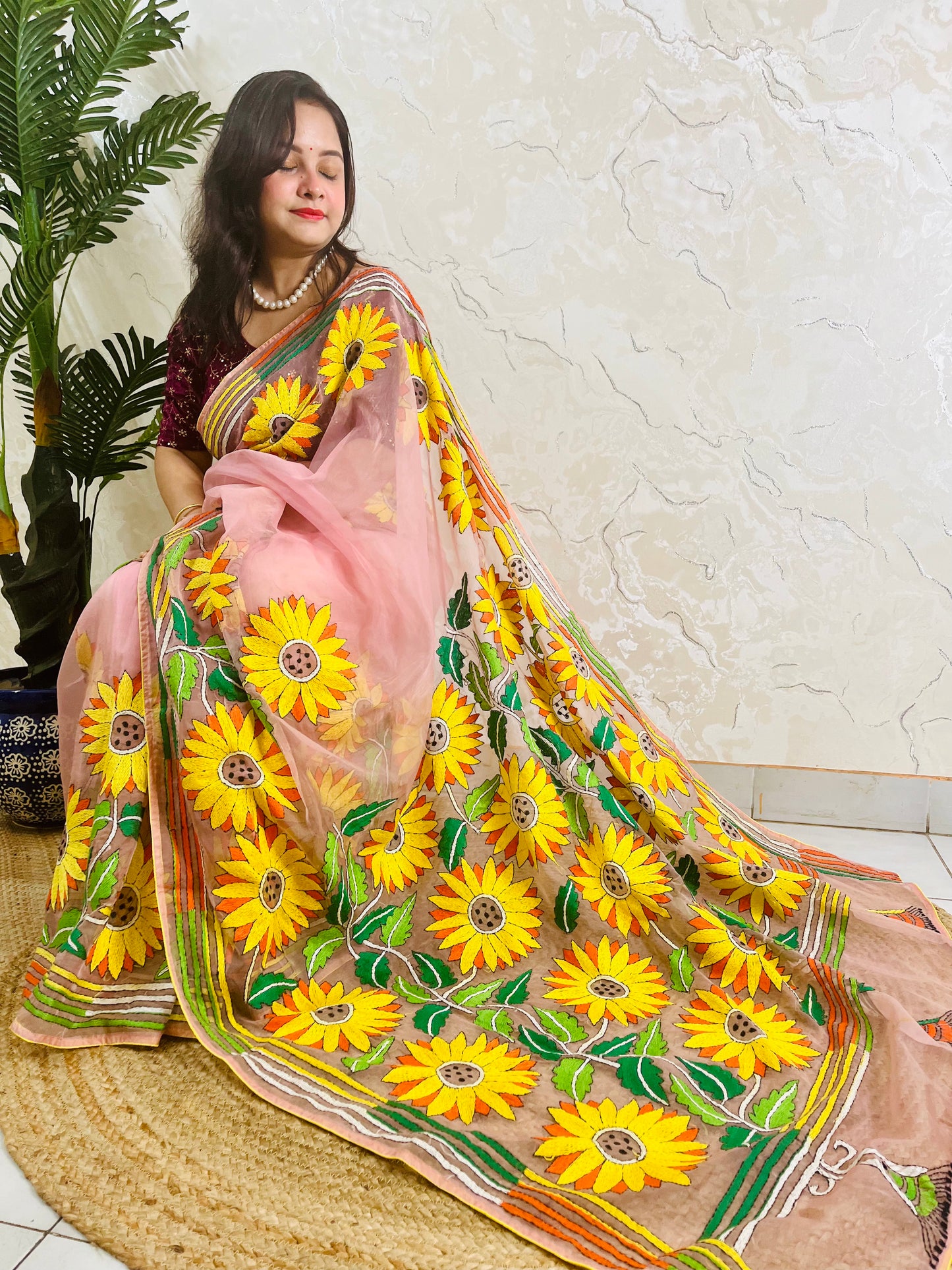 Sunflower Kantha stitch handmade blush pink organza saree with generously spaced golden yellow and orange sunflower blooms — side sitting drape view, Desi Aadat