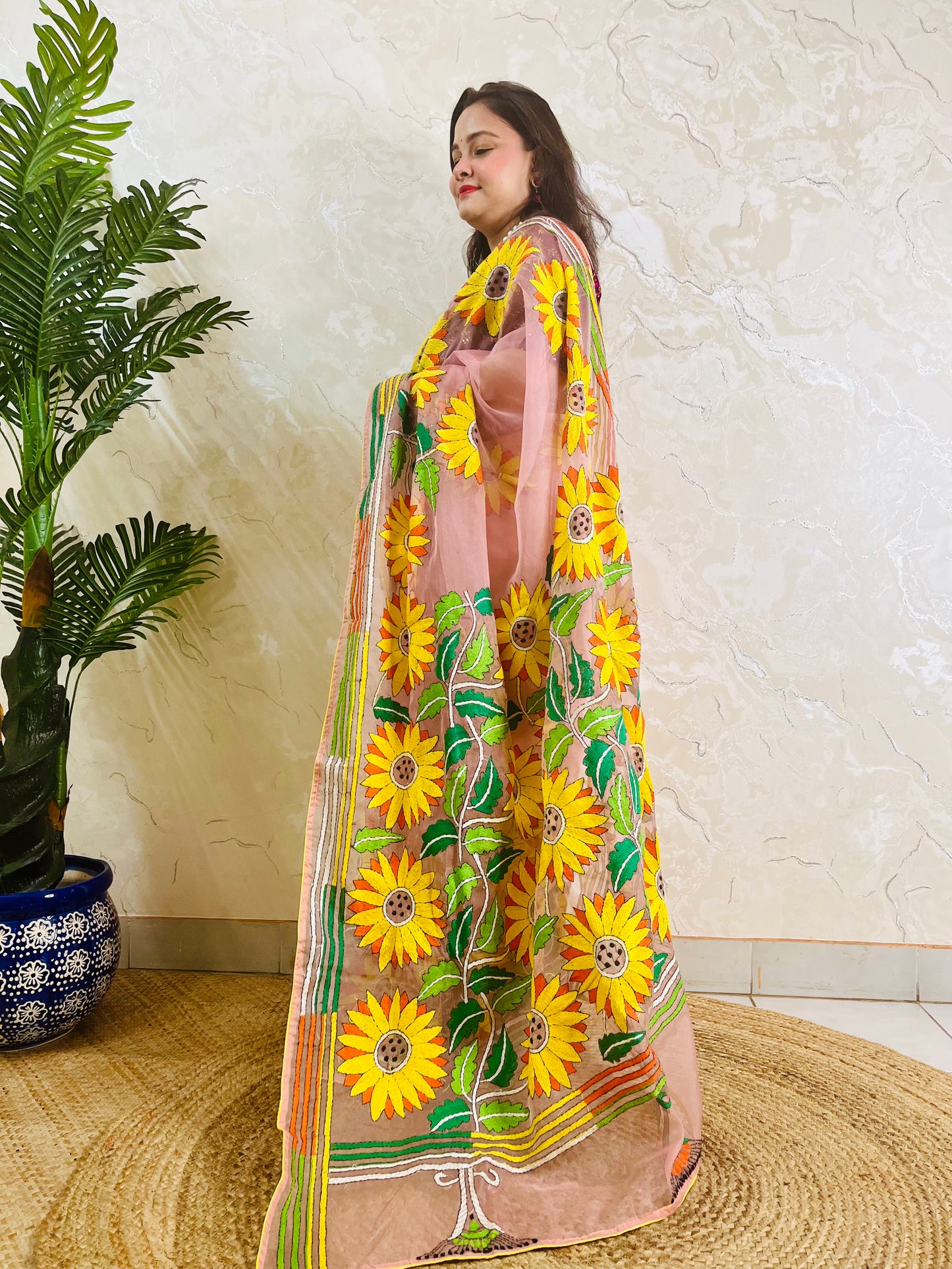 Limited edition blush pink Kantha stitch organza saree with large all-over golden sunflower embroidery and multicolour border — side standing view by Desi Aadat