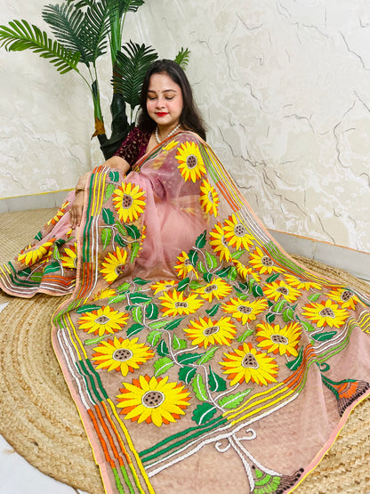 Handmade sunflower Kantha stitch blush pink organza saree with large golden yellow sunflower blooms and multicolour stripe border — angled sitting drape view, Desi Aadat