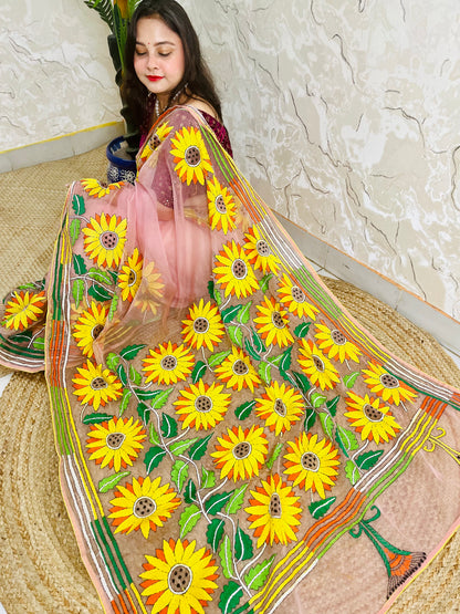 Handmade sunflower Kantha stitch blush pink organza saree with large golden yellow sunflower blooms and multicolour stripe border — angled sitting drape view, Desi Aadat