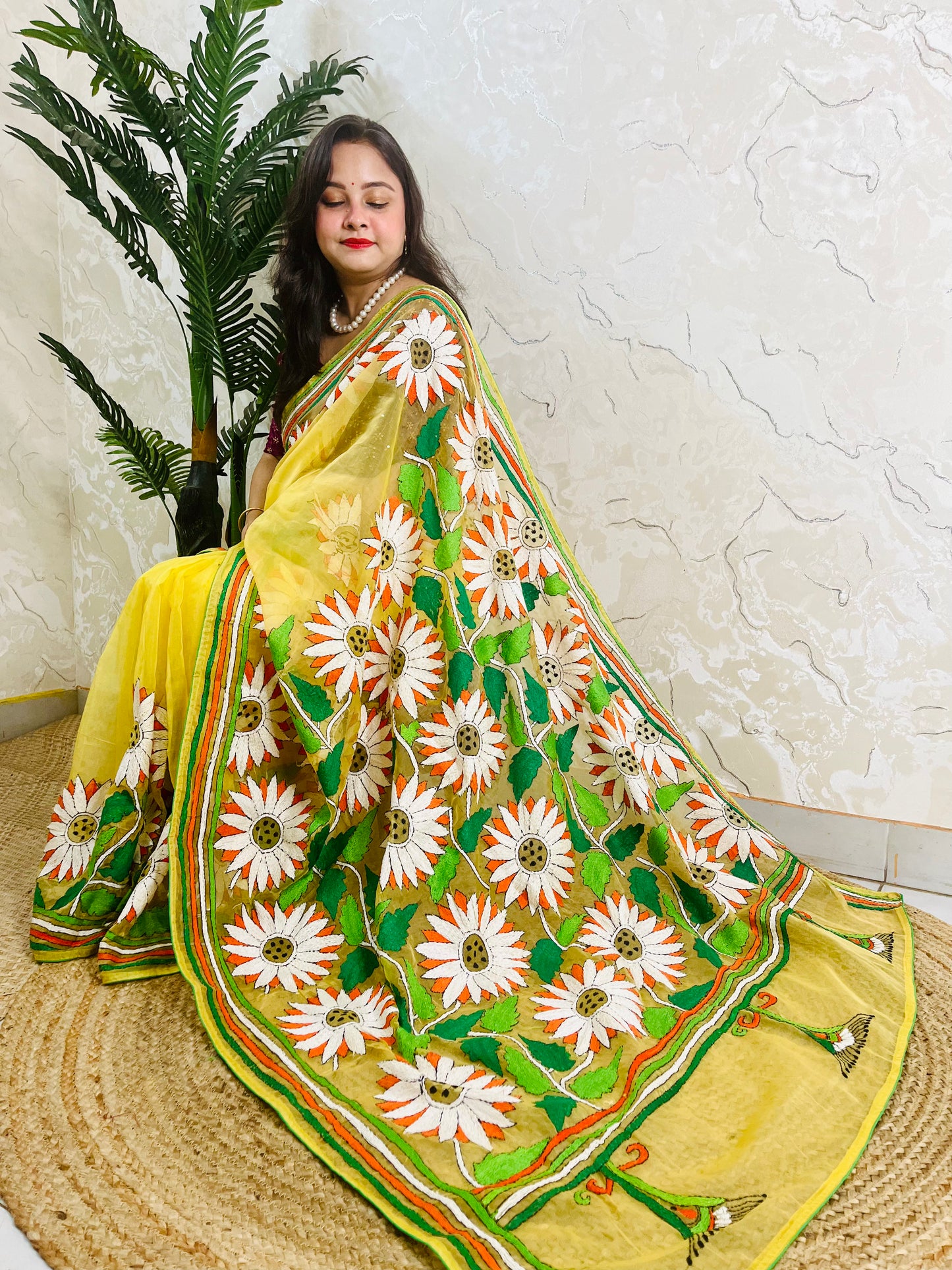 Sunflower Kantha stitch handmade sunny yellow organza saree with bold white and orange daisy blooms and green leaf embroidery — side sitting drape view, Desi Aadat