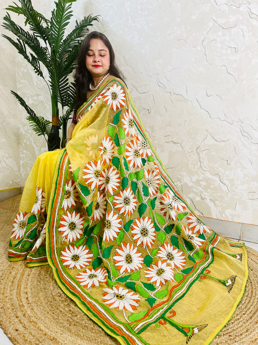 Sunflower Kantha stitch handmade sunny yellow organza saree with bold white and orange daisy blooms and green leaf embroidery — side sitting drape view, Desi Aadat