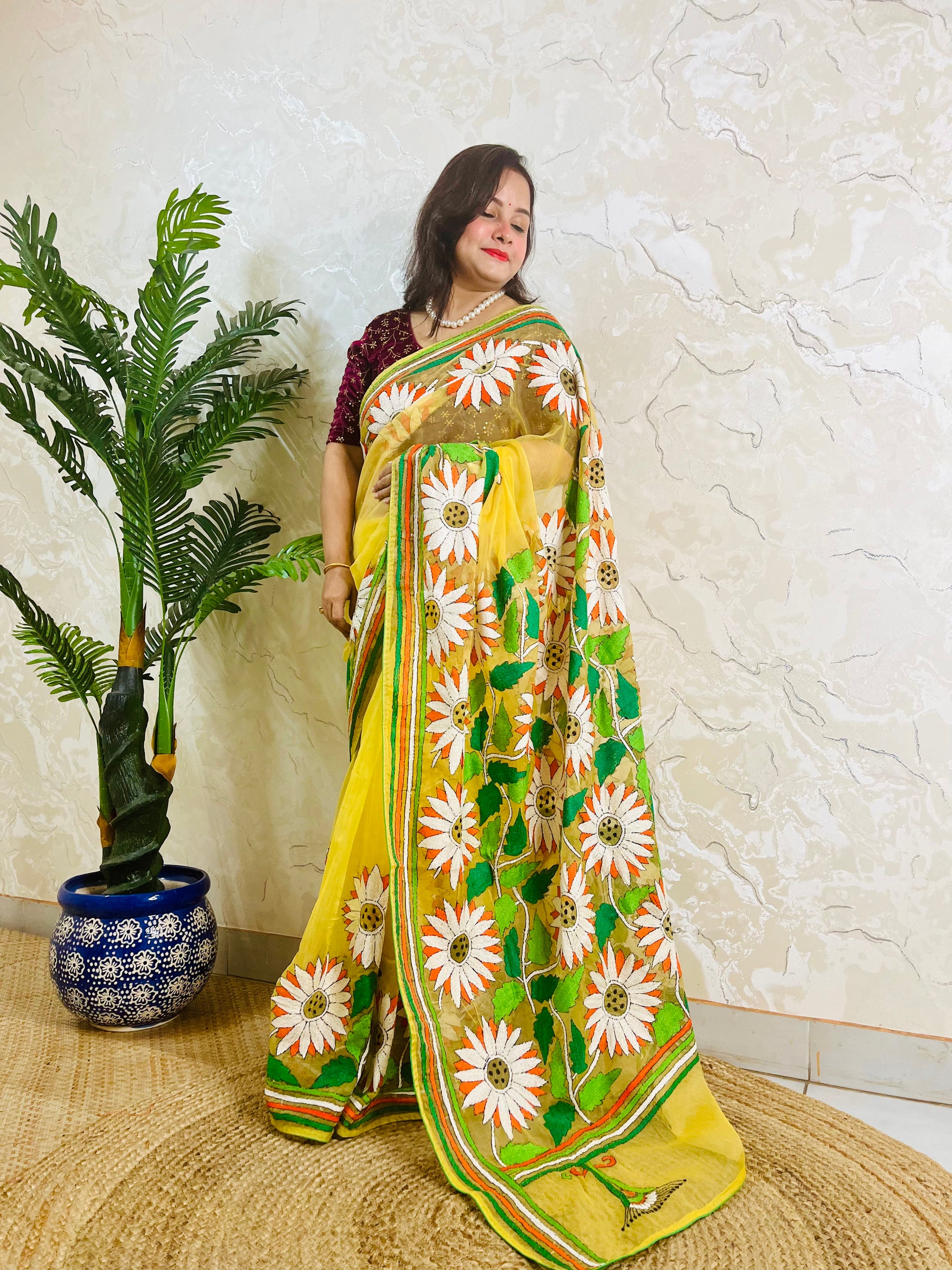 Handmade sunflower Kantha stitch sunny yellow organza saree with white daisy blooms, orange petals, green leaves, and multicolour stripe border — standing view, Desi Aadat