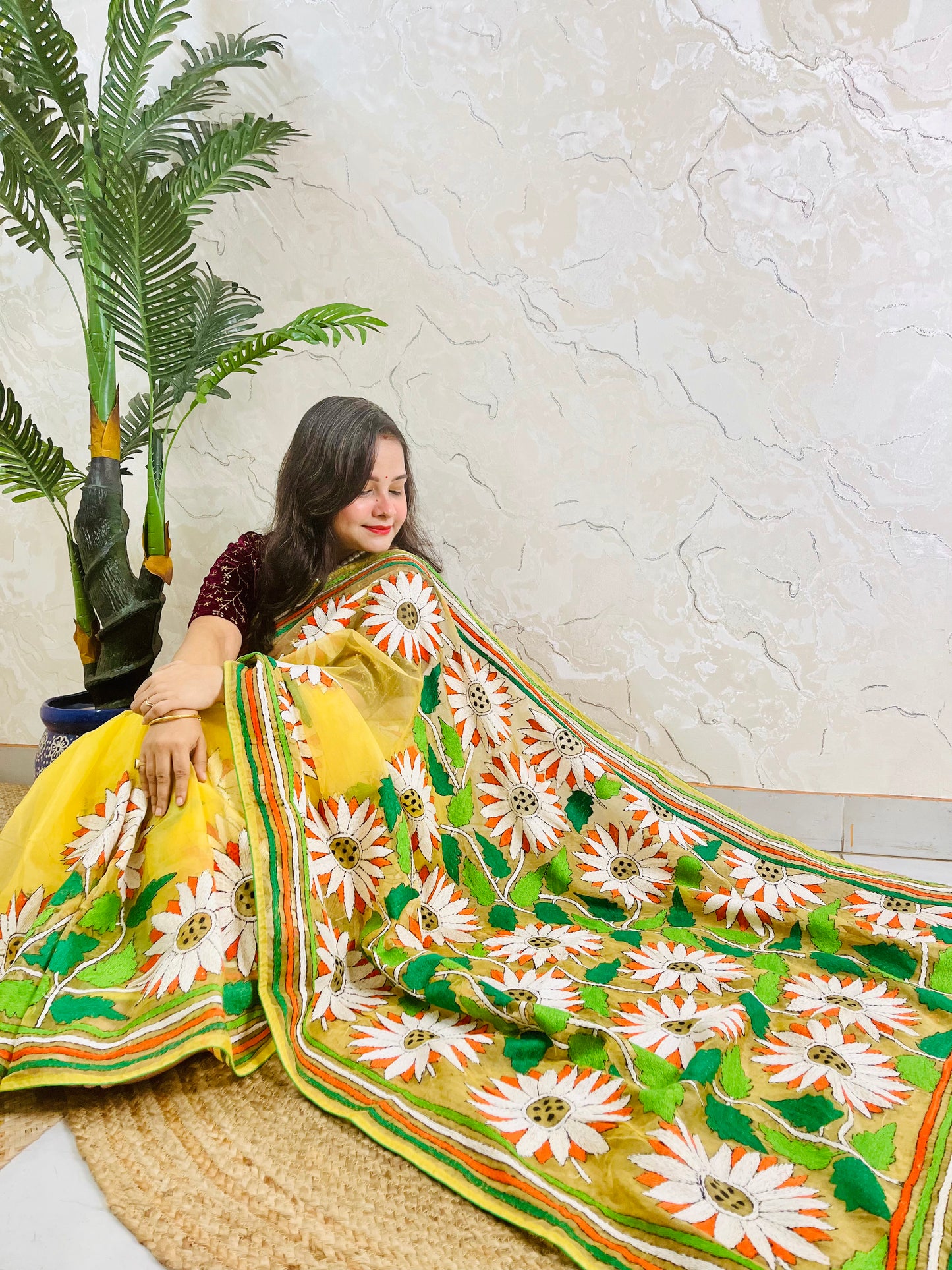 Sunny yellow organza saree with Bengal Kantha stitch white sunflower embroidery and hummingbird border motif displayed in low side sitting view — Desi Aadat