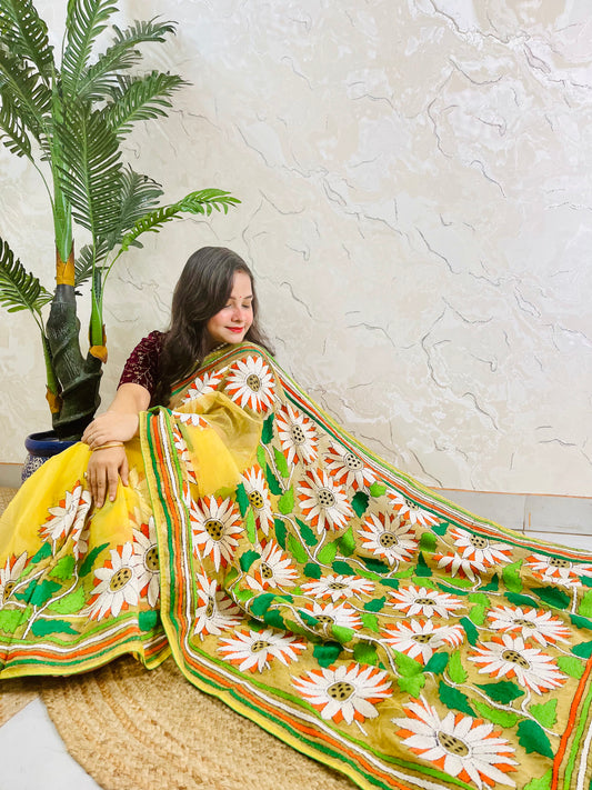 Sunny yellow organza saree with Bengal Kantha stitch white sunflower embroidery and hummingbird border motif displayed in low side sitting view — Desi Aadat