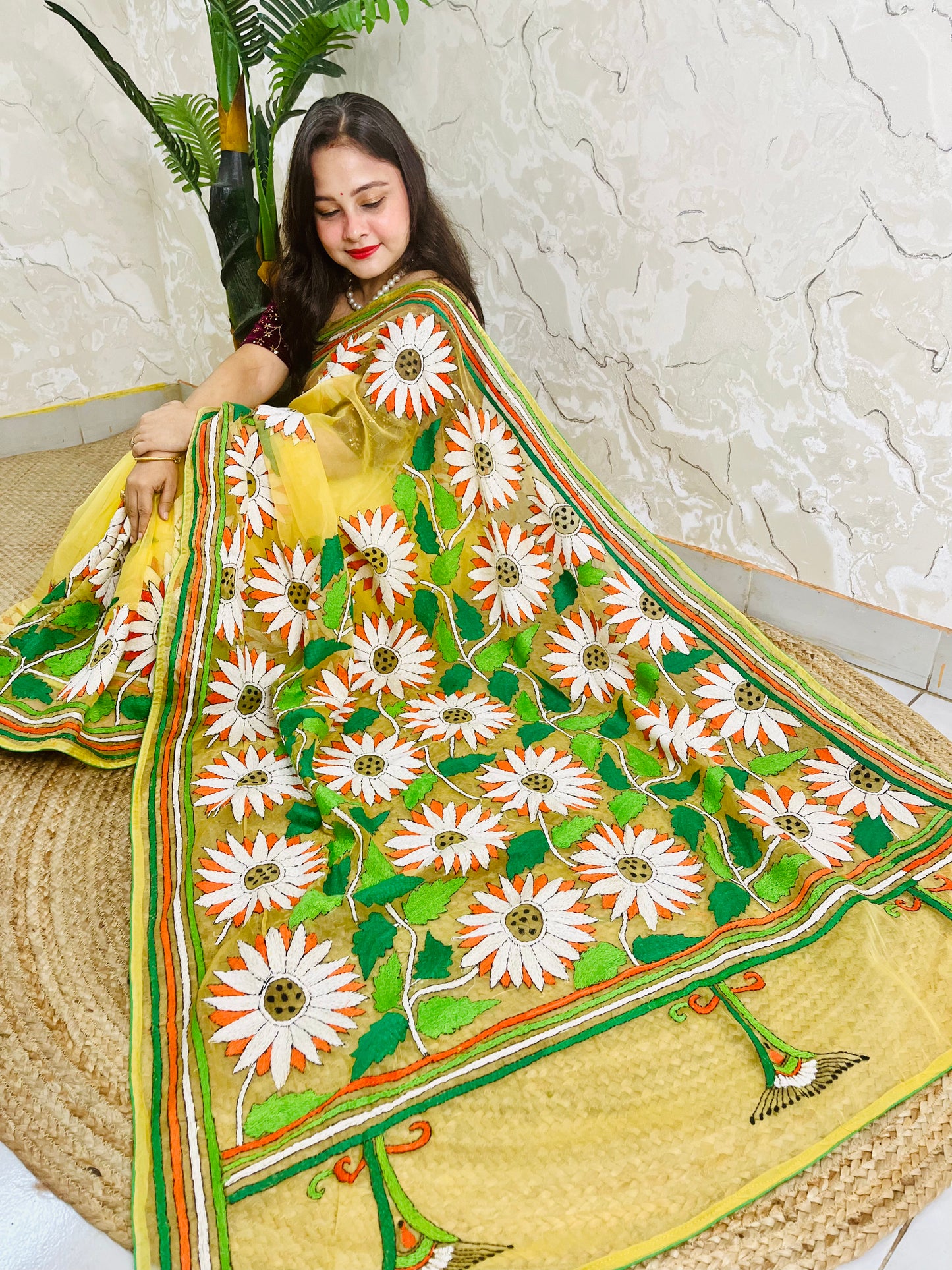 Sunny yellow organza saree with Bengal Kantha stitch white sunflower embroidery and hummingbird border motif displayed in low side sitting view — Desi Aadat