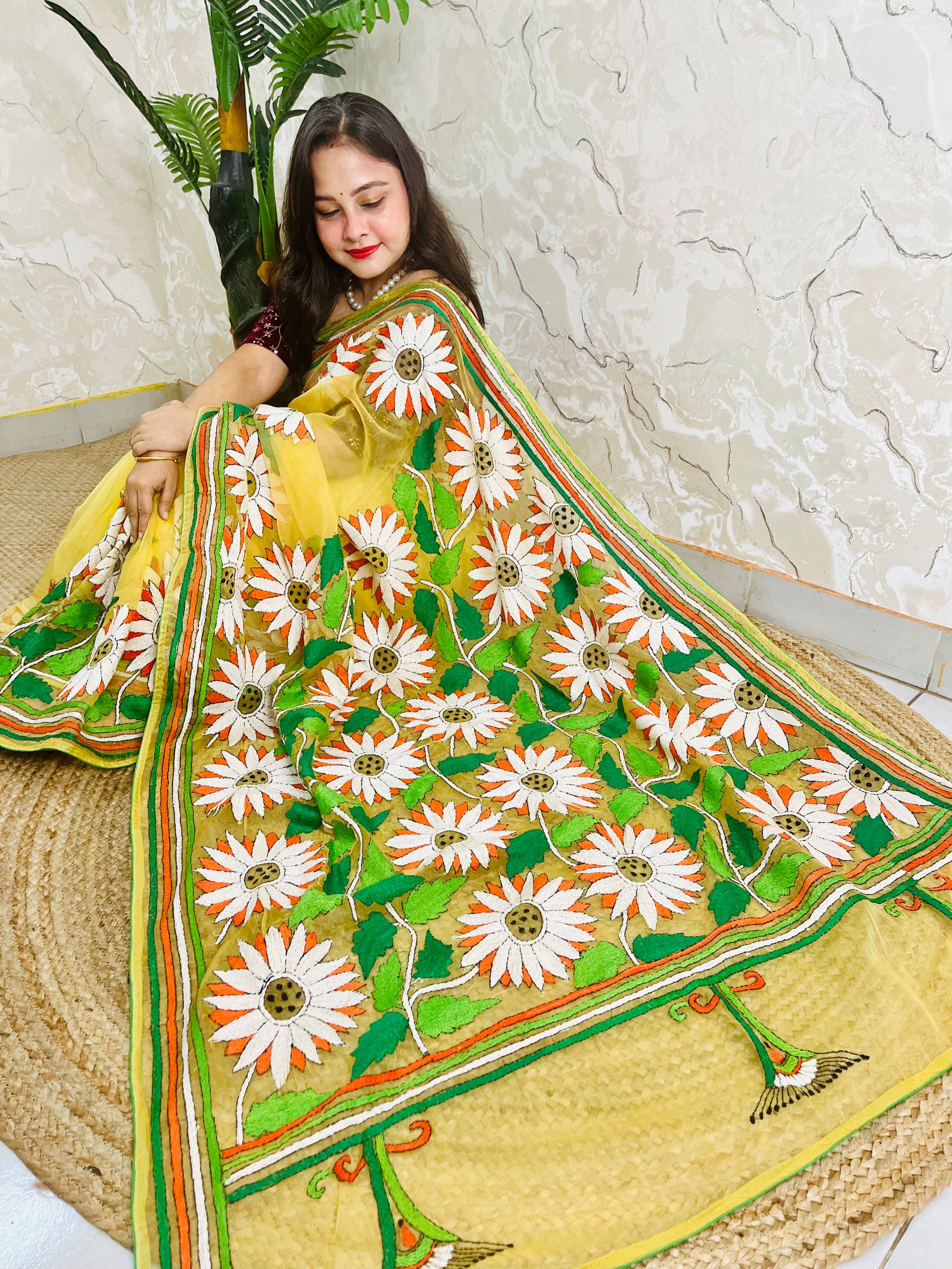 Sunny yellow organza saree with Bengal Kantha stitch white sunflower embroidery and hummingbird border motif displayed in low side sitting view — Desi Aadat