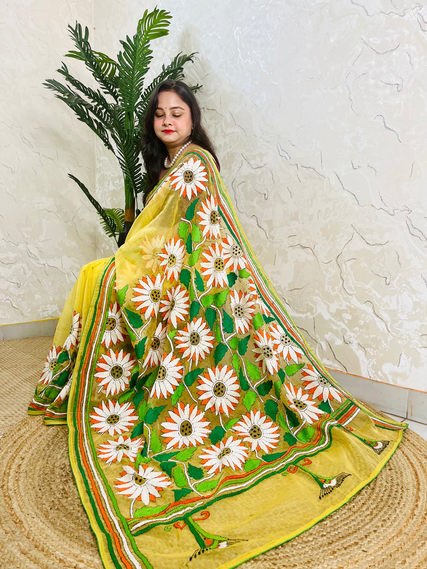 Sunflower Kantha stitch handmade sunny yellow organza saree with bold white and orange daisy blooms and green leaf embroidery — side sitting drape view, Desi Aadat