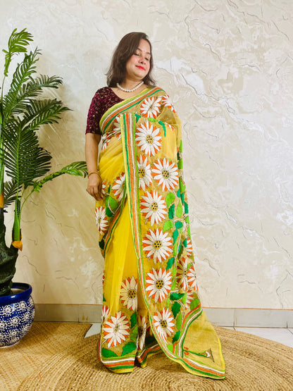 Handmade sunflower Kantha stitch sunny yellow organza saree with white daisy blooms, orange petals, green leaves, and multicolour stripe border — standing view, Desi Aadat