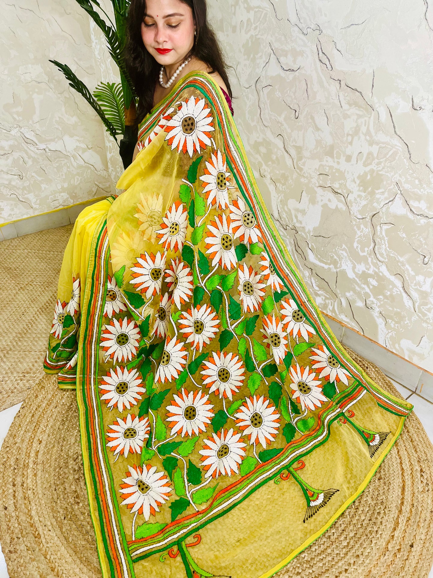 Sunflower Kantha stitch handmade sunny yellow organza saree with bold white and orange daisy blooms and green leaf embroidery — side sitting drape view, Desi Aadat