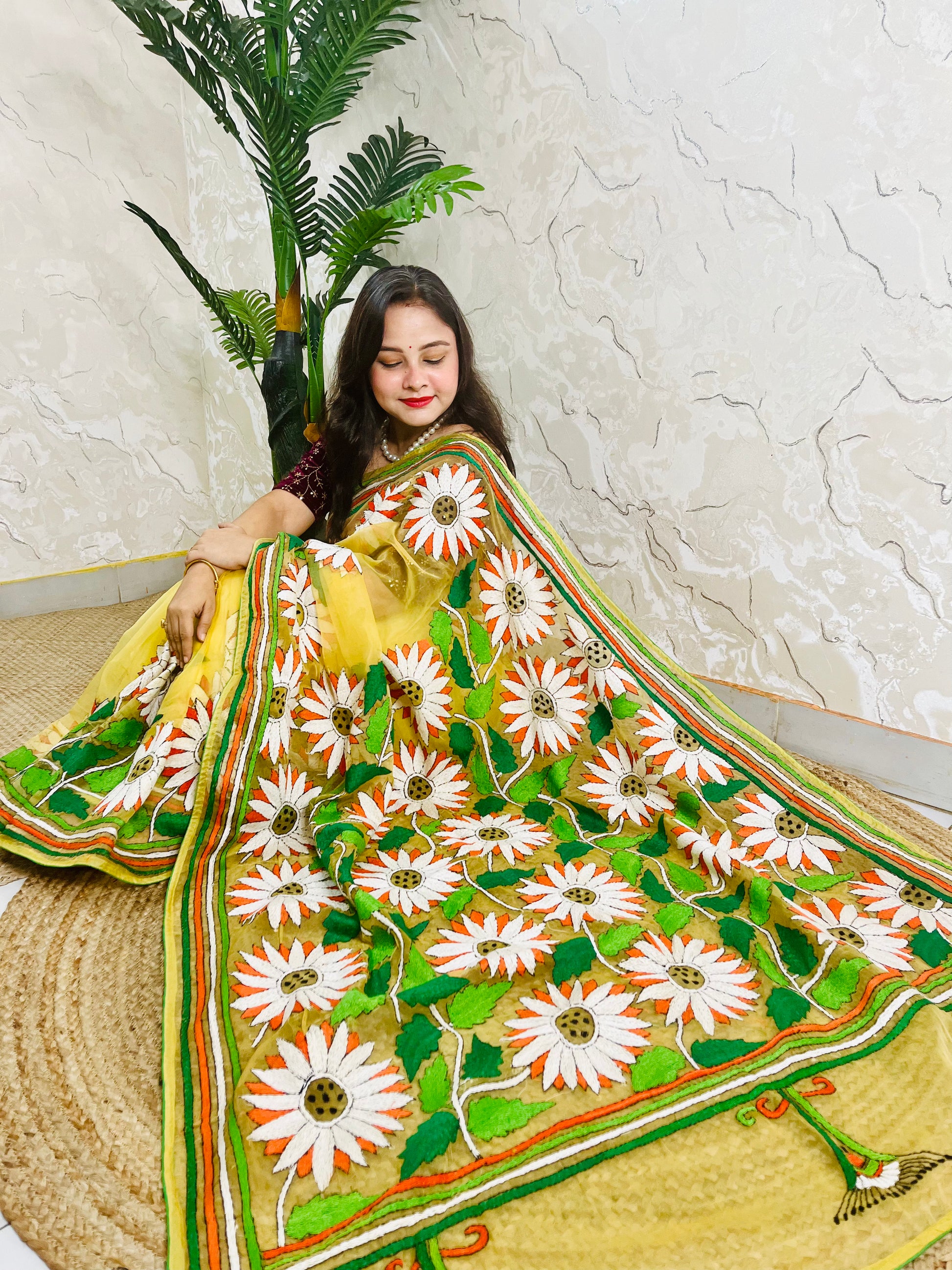 Sunny yellow organza saree with Bengal Kantha stitch white sunflower embroidery and hummingbird border motif displayed in low side sitting view — Desi Aadat