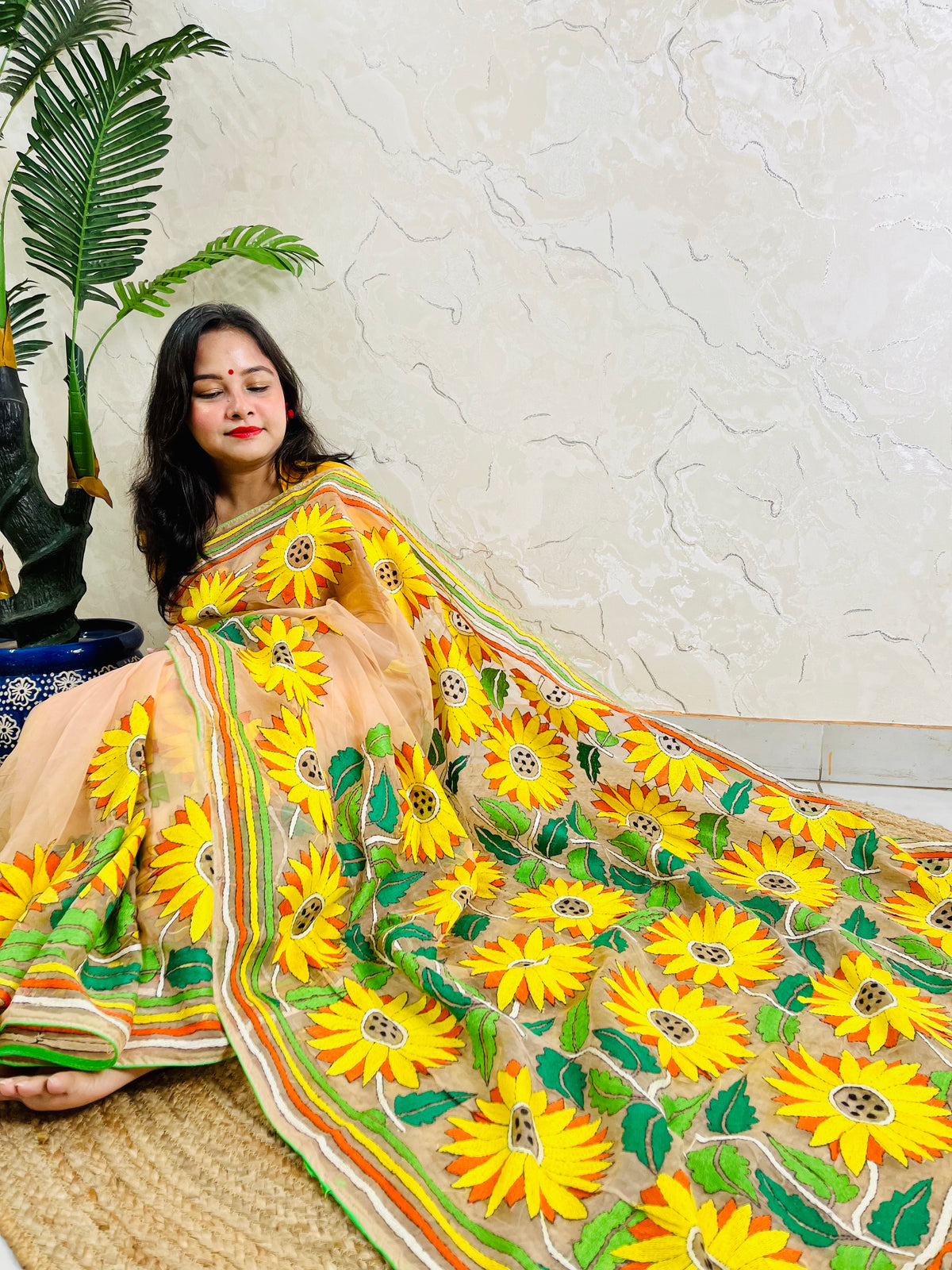 Woman seated in light peach sunflower Kantha stitch saree, top view