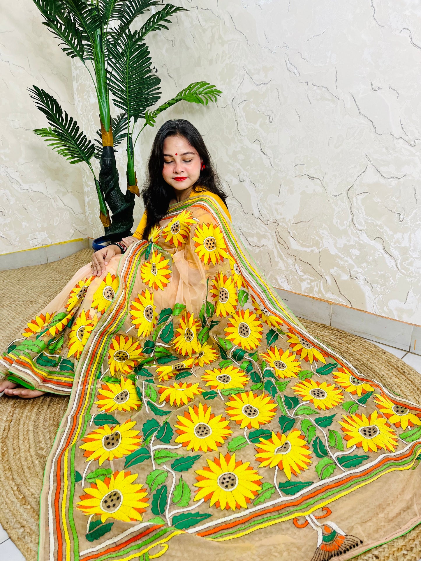 Woman seated in light peach sunflower Kantha stitch saree, top view