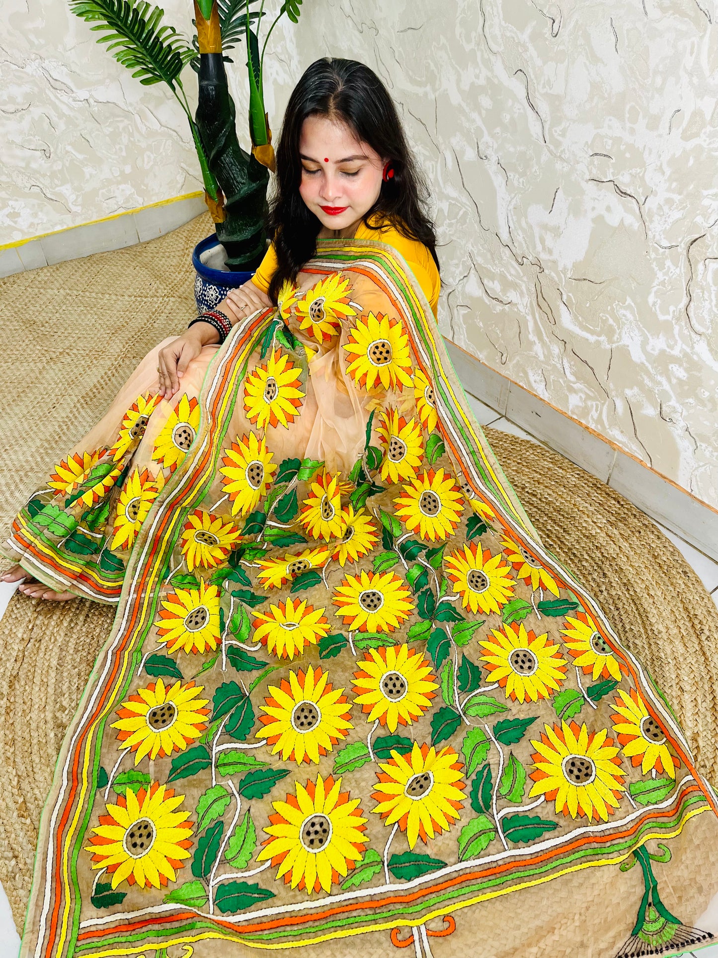 Woman seated in light peach sunflower Kantha stitch saree, top view