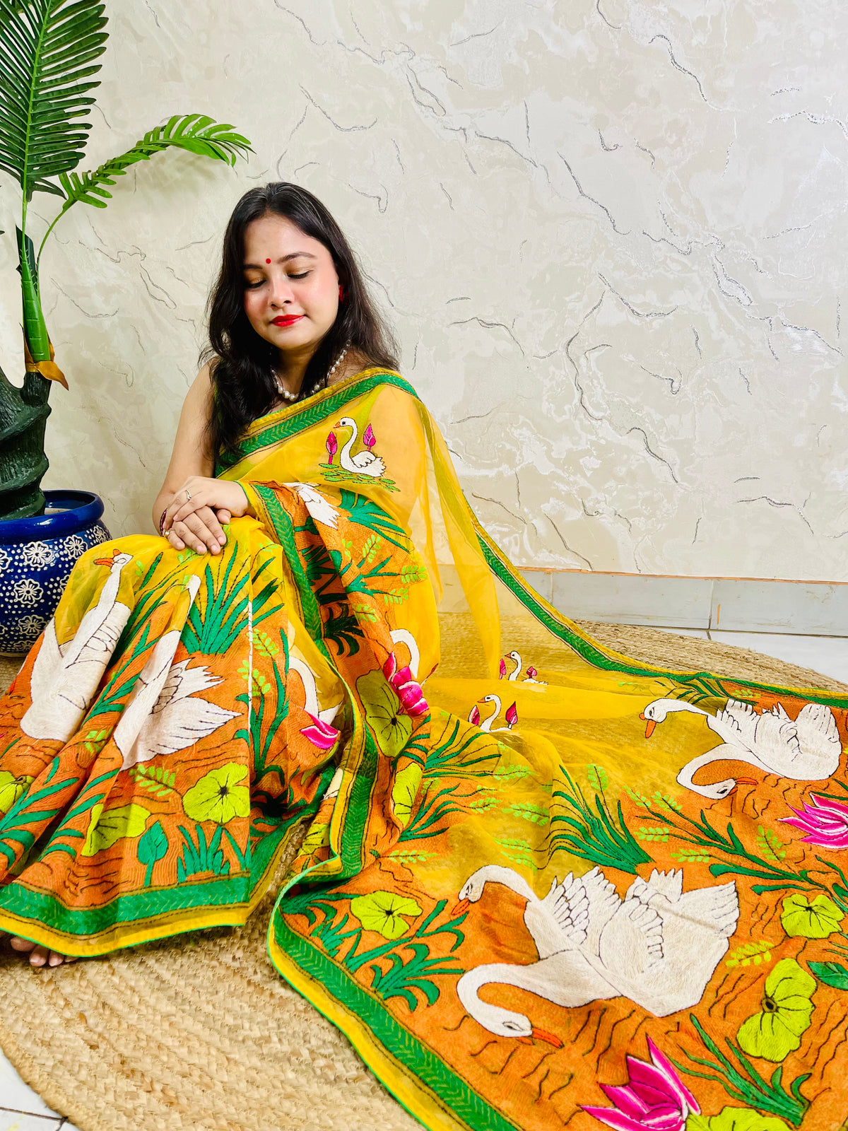 Woman seated in sunshine yellow organza saree with swan embroidery