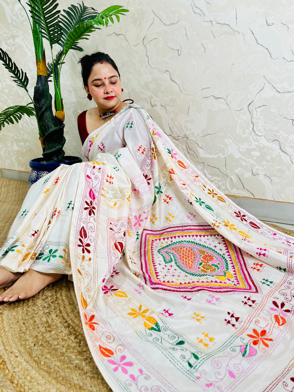 Woman seated in white Kantha stitch saree with paisley pallu spread out