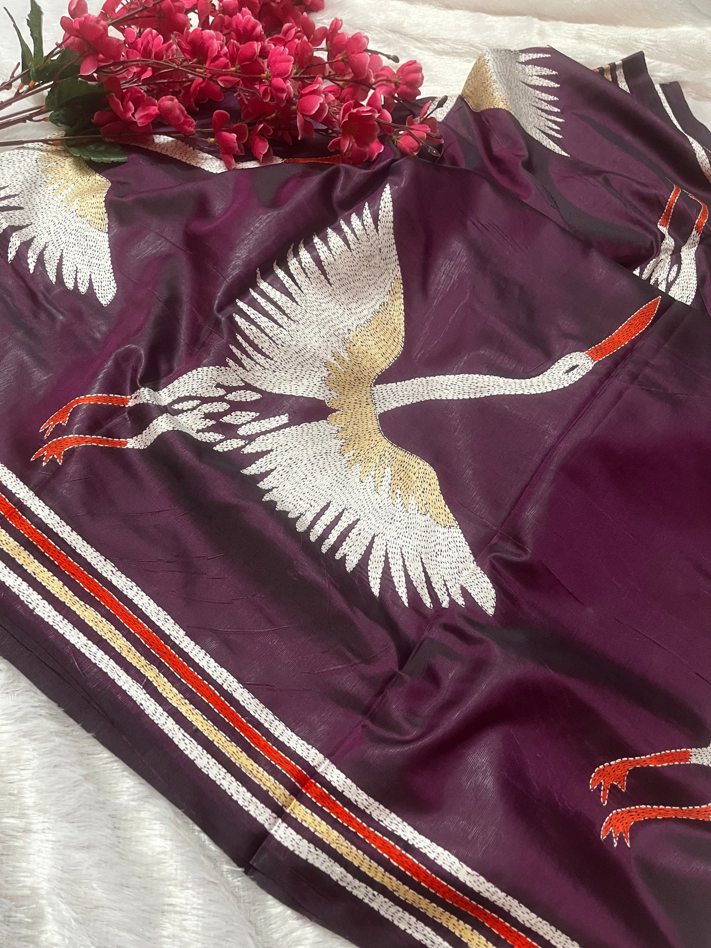 Close-up of handcrafted kantha stitch embroidery showing crane motifs on wine fabric